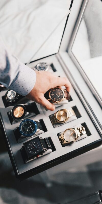 A sophisticated display of luxury watches in an elegant case with a hand selecting one.