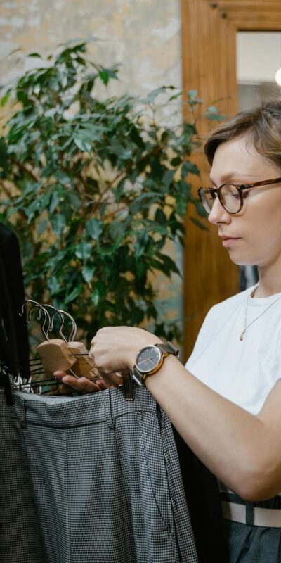 Woman with eyeglasses shopping for trousers in a stylish boutique with indoor plants.