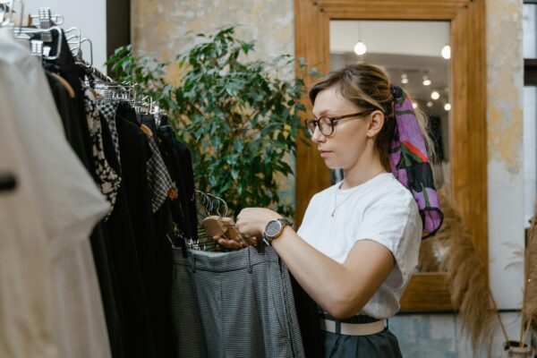 Woman with eyeglasses shopping for trousers in a stylish boutique with indoor plants.